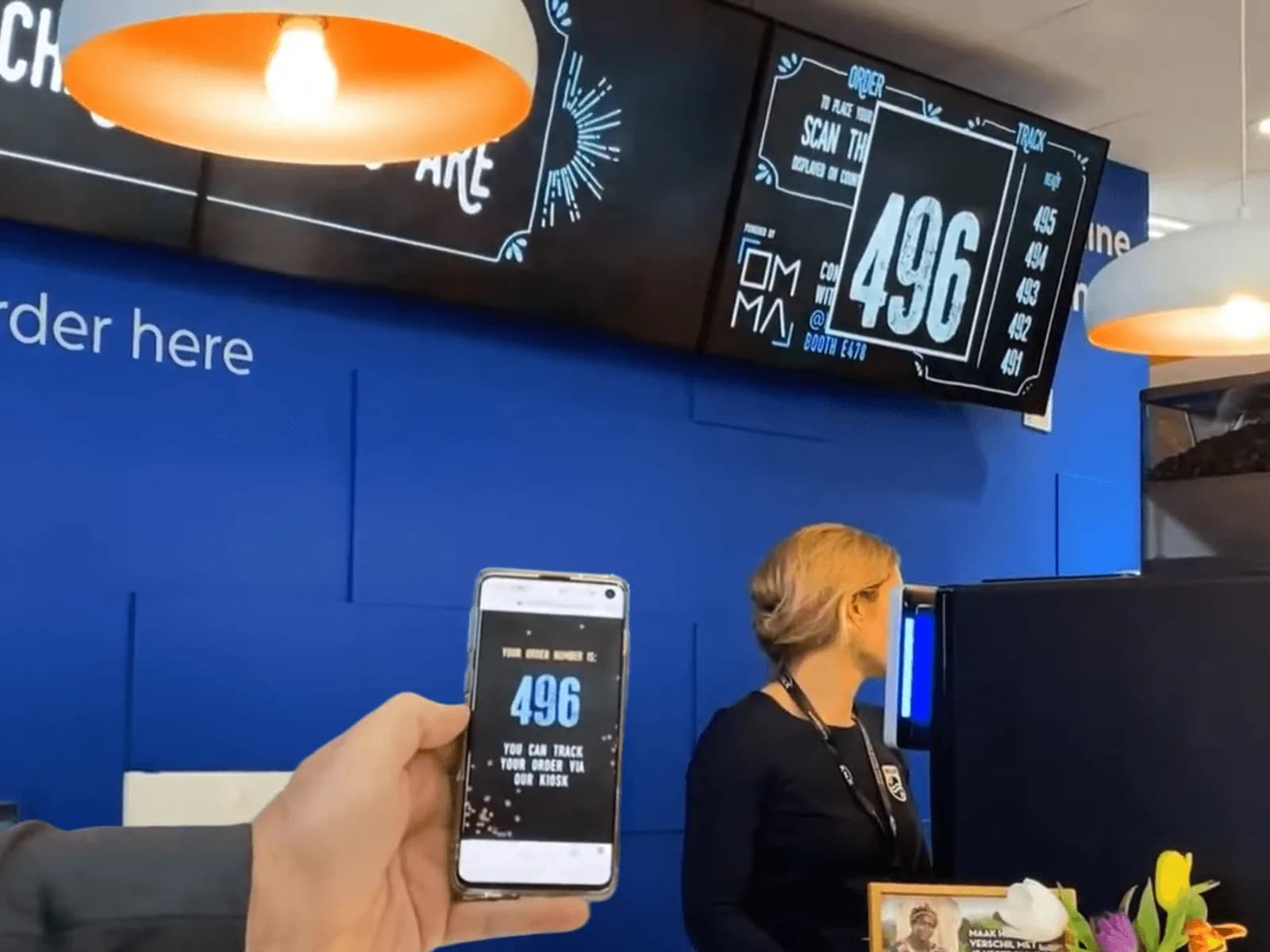 The 'Coffee on Tap' coffee corner at the Philips booth, overhead menu board, live order number, and the barista at the counter
