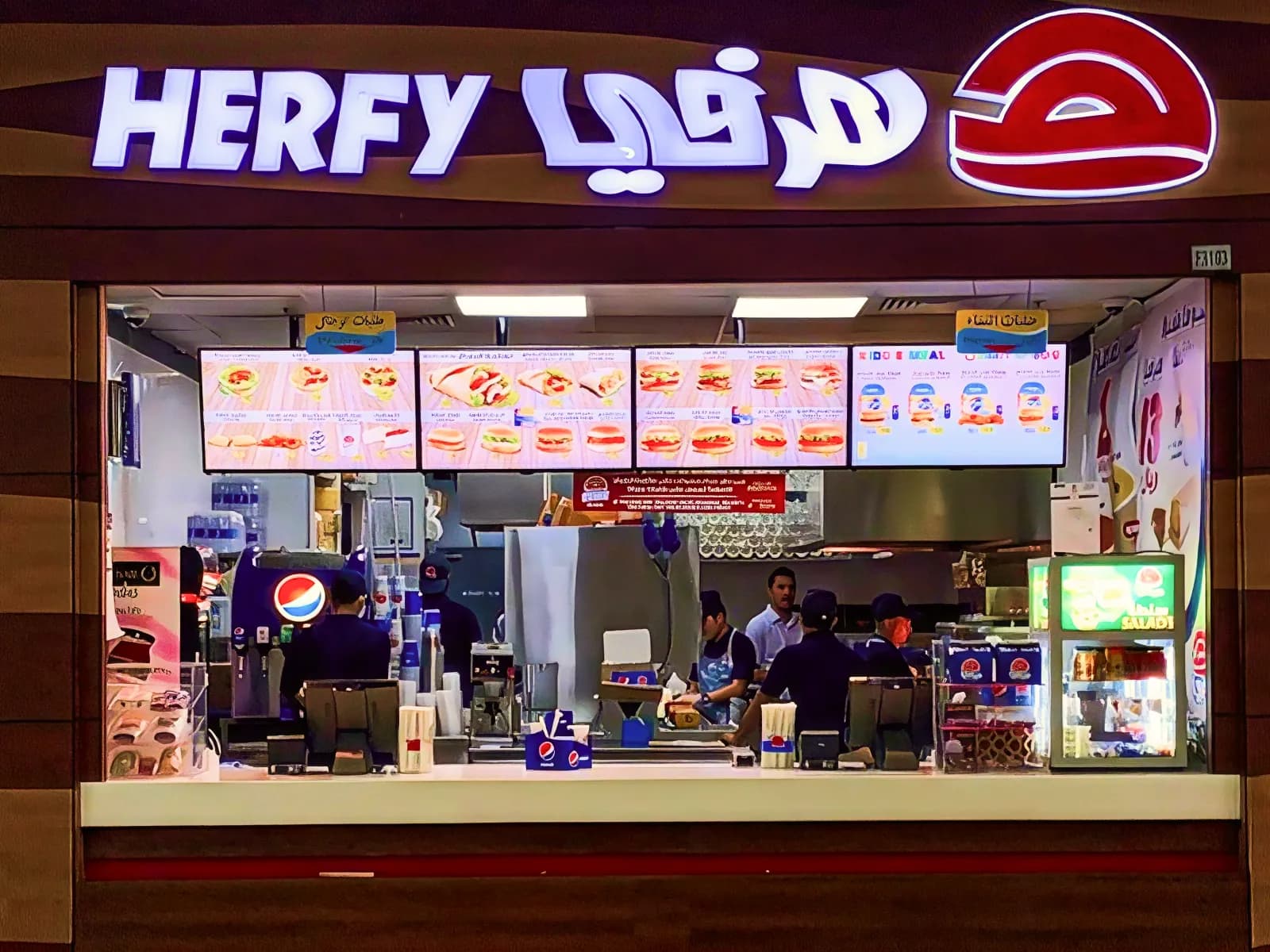 A Herfy counter in a mall food court, with a row of four menuboards above the kitchen