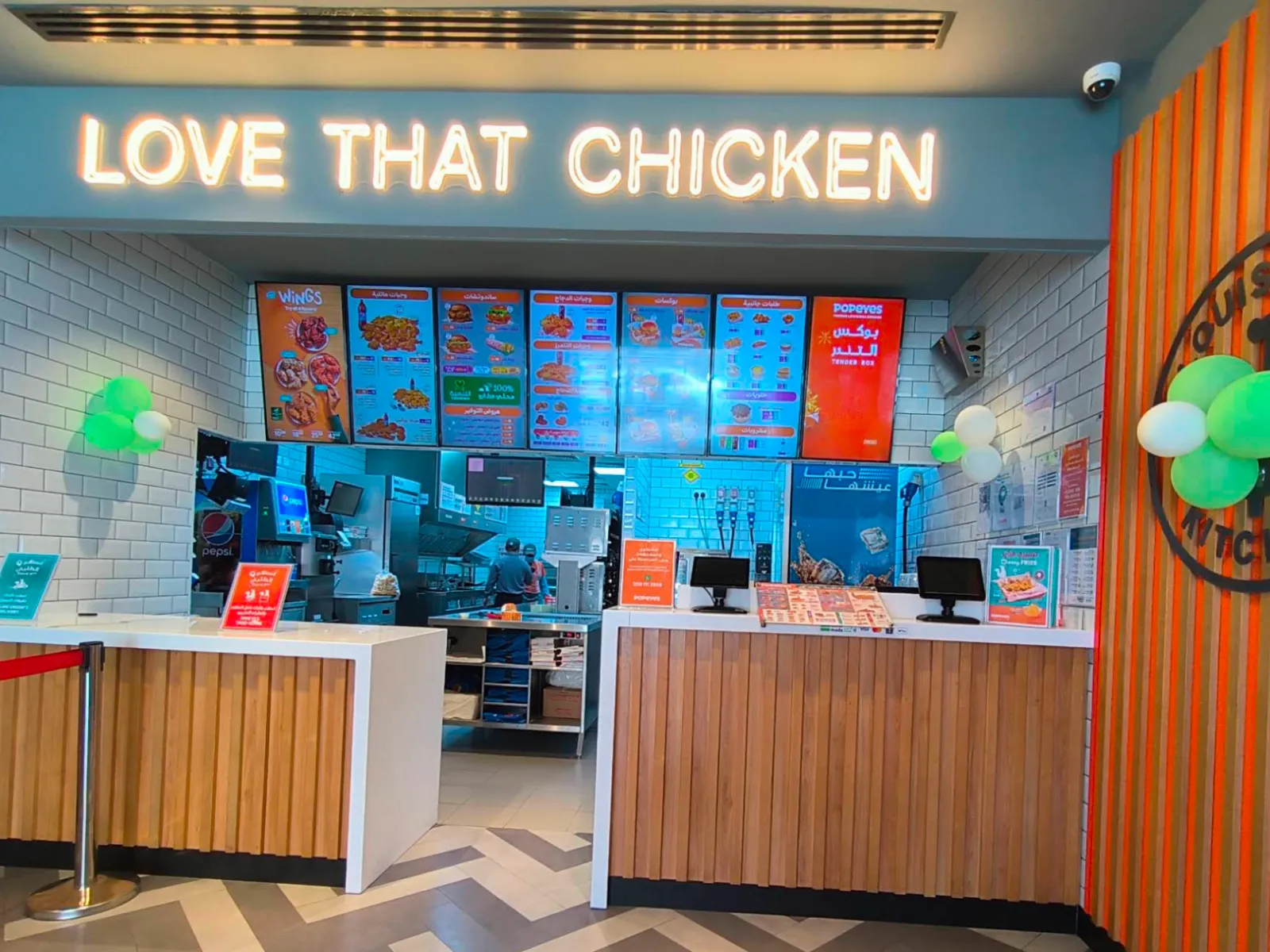 Seven menuboards in a row above a Popeyes counter, under a lit sign reading Love That Chicken