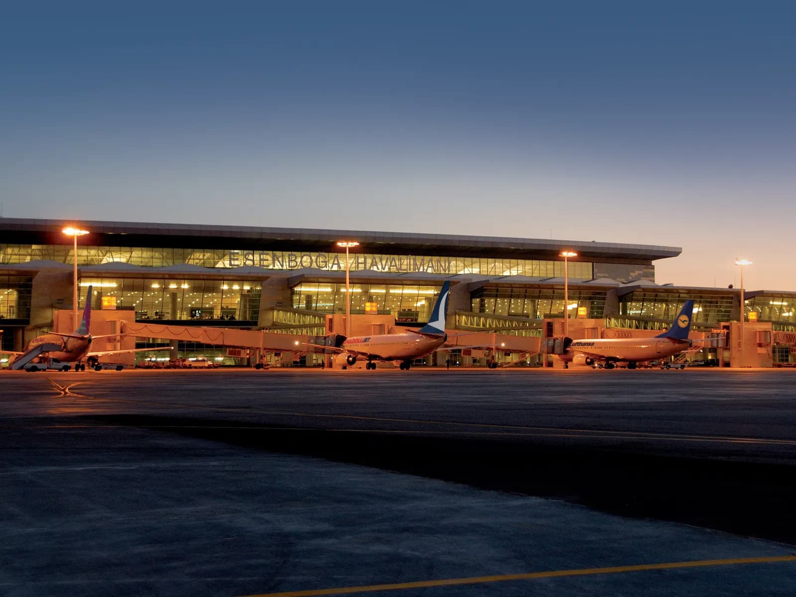 Ankara Esenboğa Airport's terminal at dusk, seen from the apron with aircraft at the gates
