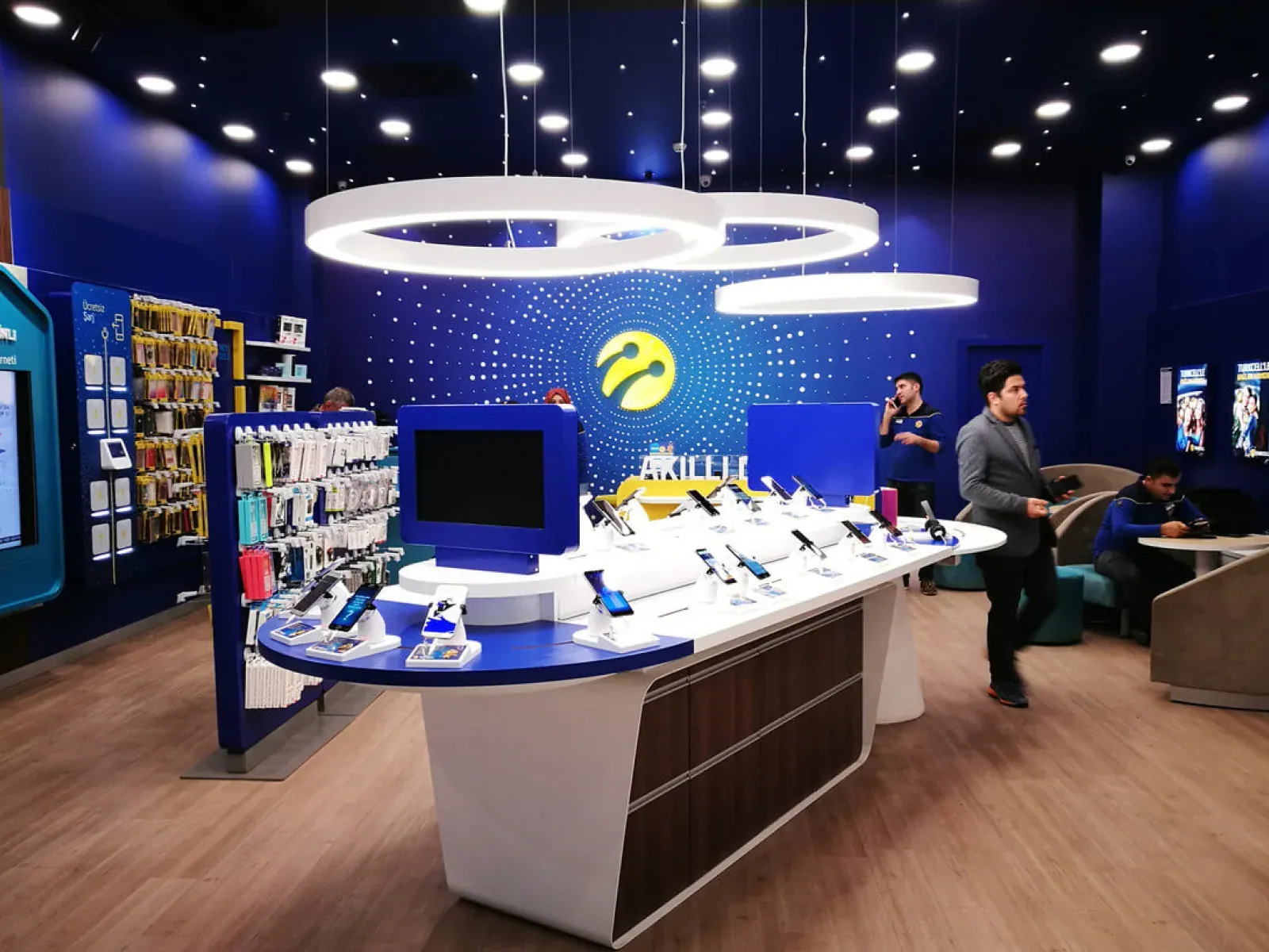 Inside a Turkcell store: the illuminated Turkcell symbol on a deep-blue wall above a product table of live OmmaSign screens