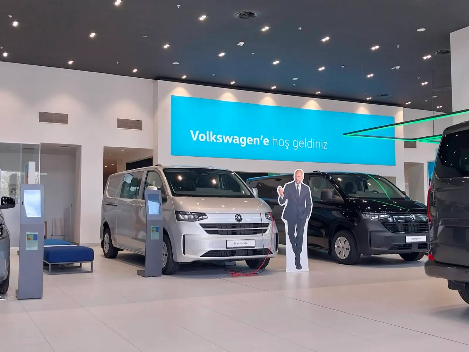 A Volkswagen showroom with a wide welcome screen above two Transporter vans and two pedestal screens on the floor
